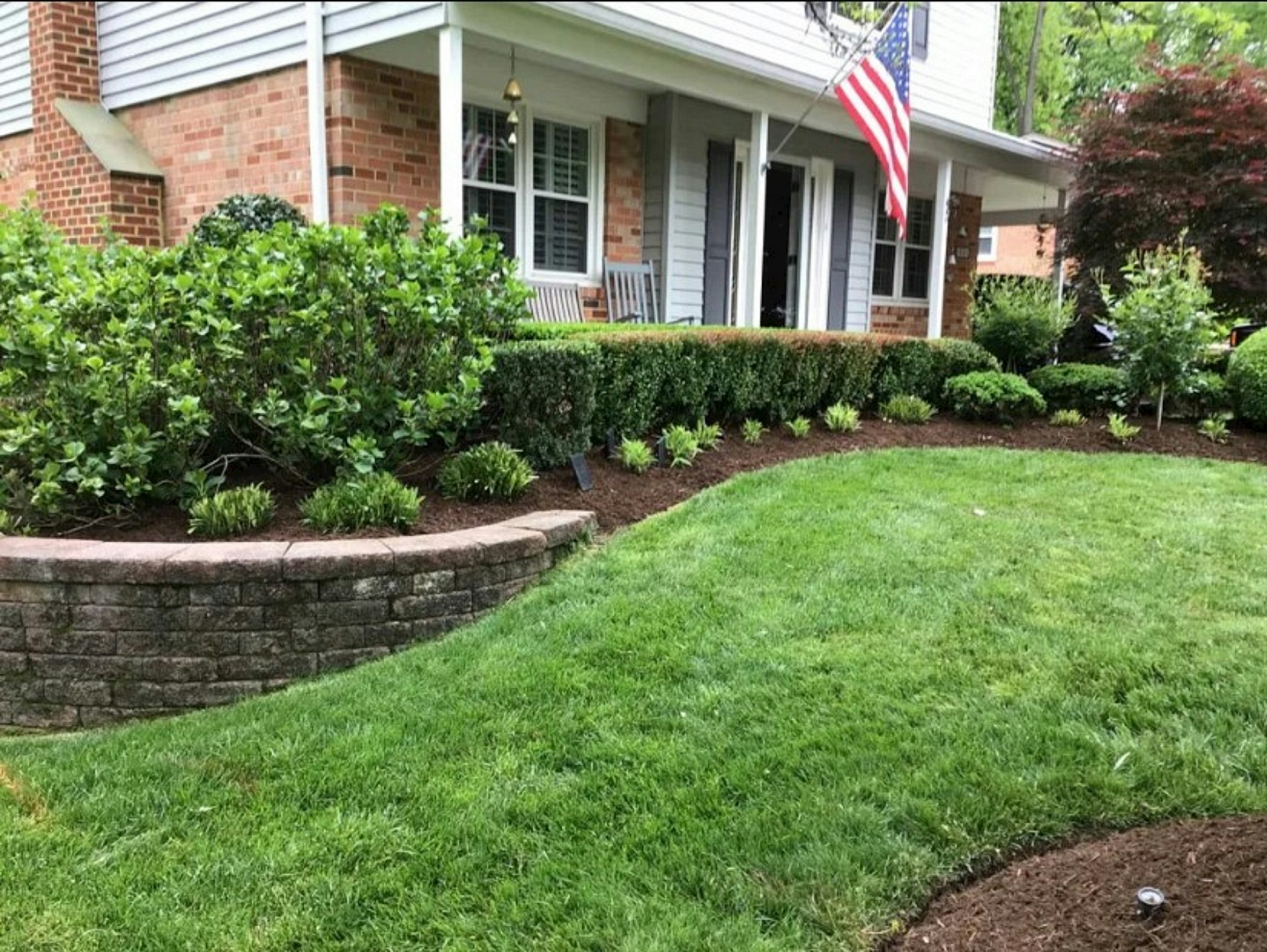 Well-maintained brick home with landscaped front yard, hedges, and lush green lawn