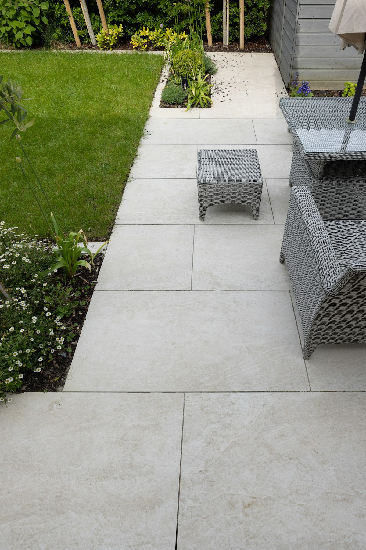 Modern patio with light gray stone pavers, wicker furniture, and manicured lawn border