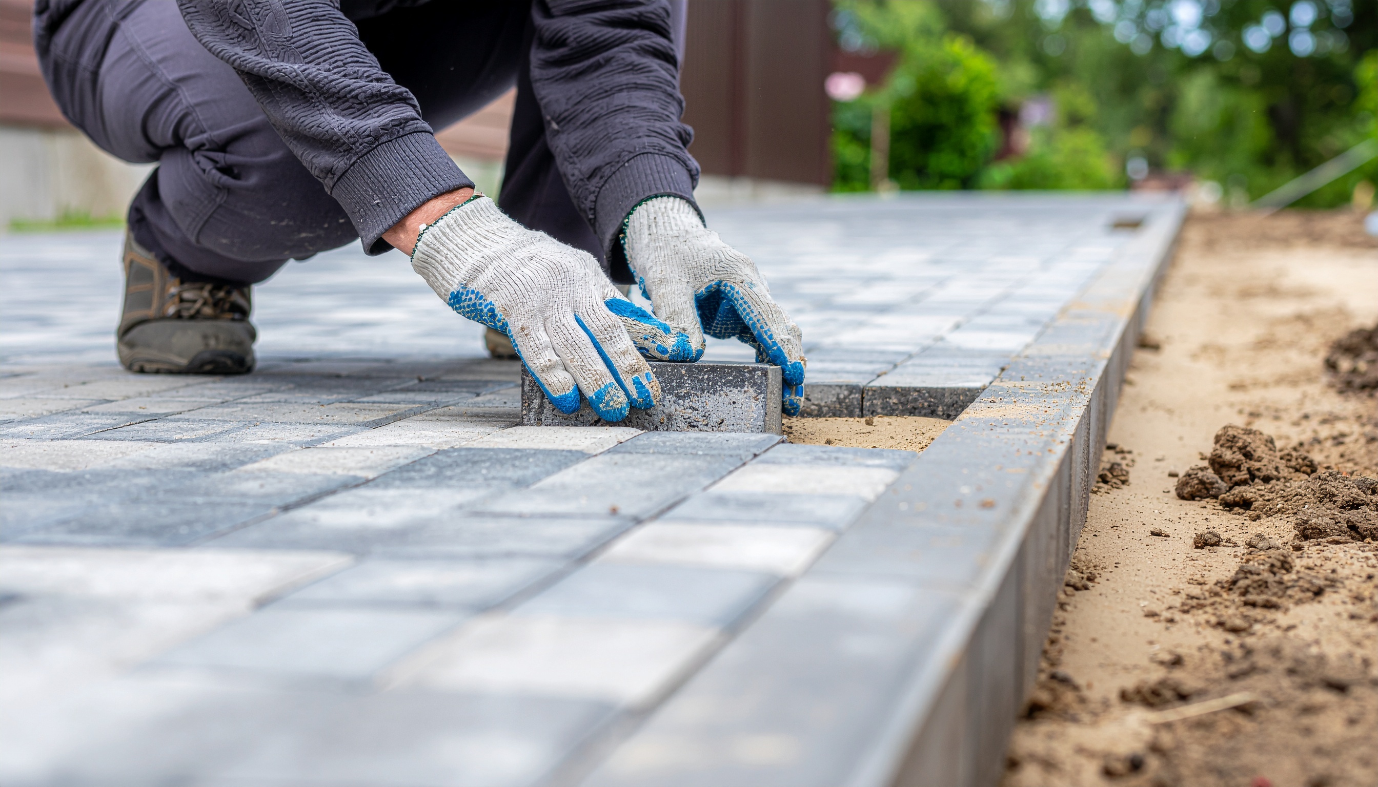 Worker laying paving stones in work gloves and boots during outdoor construction